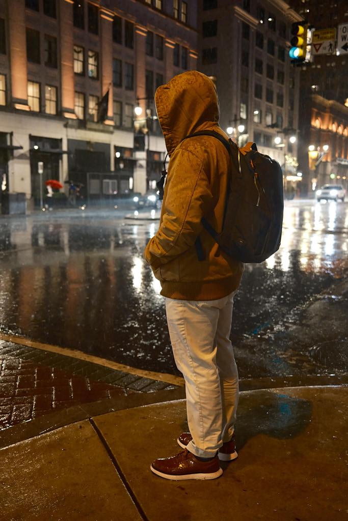 Man standing on a street corner in the rain.