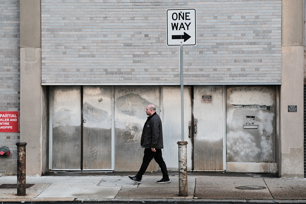 Man walking in the opposite direction pointed to by a One Way sign.